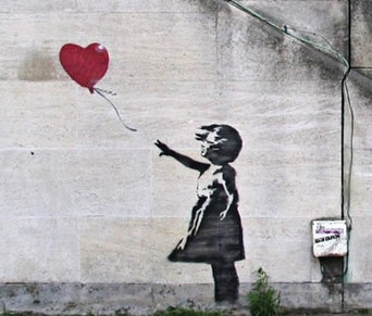 Girl with Balloon by Banksy, a girl stencilled in black on a concrete wall reaching towards a red heart-shaped balloon drifting out of her hand.